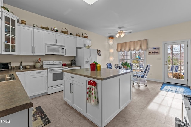 kitchen with dark countertops, white appliances, white cabinetry, and glass insert cabinets