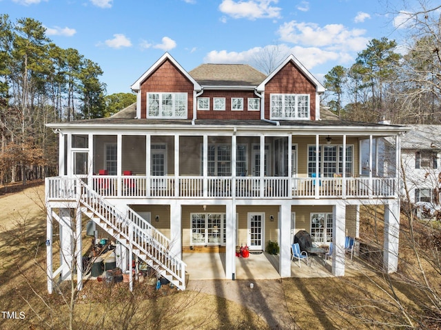 rear view of property featuring stairs, a patio, a sunroom, and roof with shingles