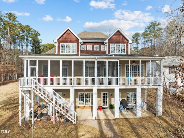 back of property featuring stairway, roof with shingles, a patio, and a sunroom