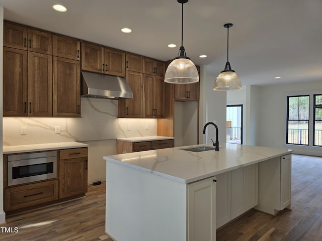 kitchen with dark wood finished floors, stainless steel microwave, under cabinet range hood, and a sink