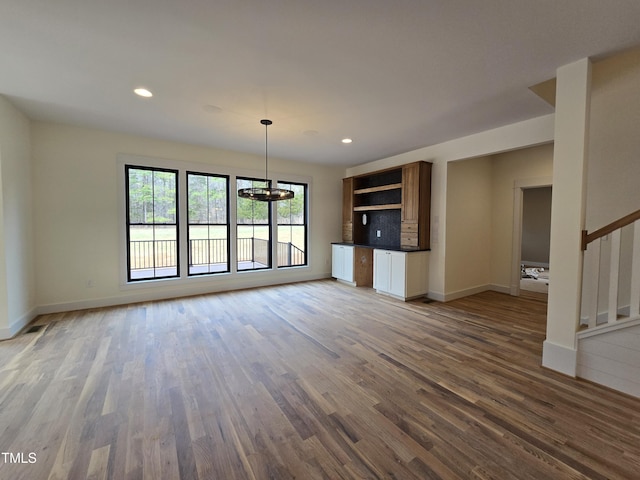 unfurnished living room with recessed lighting, baseboards, wood finished floors, and stairs