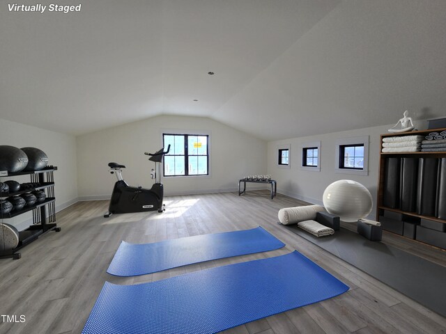 exercise area featuring baseboards, lofted ceiling, and wood finished floors