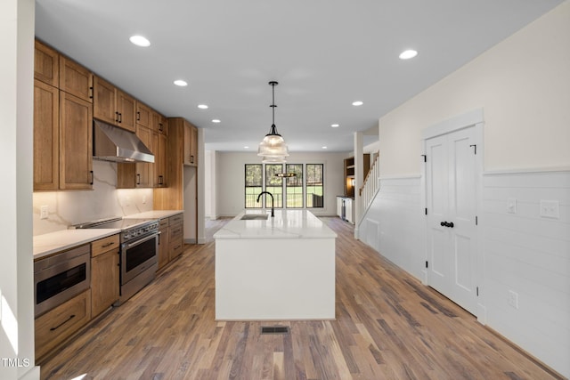 kitchen featuring a sink, stainless steel appliances, under cabinet range hood, and wood finished floors