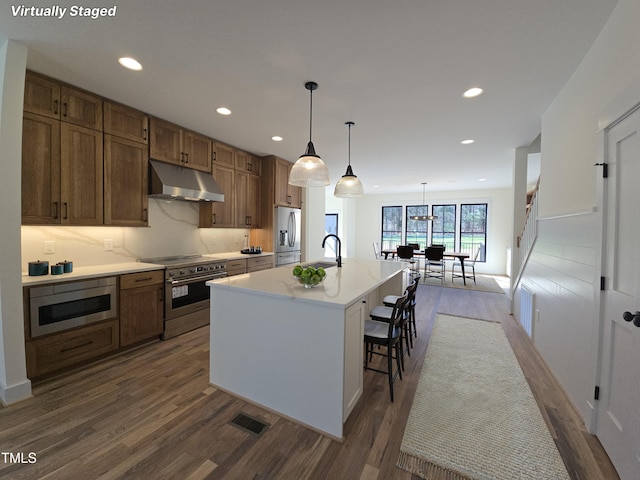 kitchen with visible vents, a kitchen island with sink, stainless steel appliances, under cabinet range hood, and dark wood-style floors