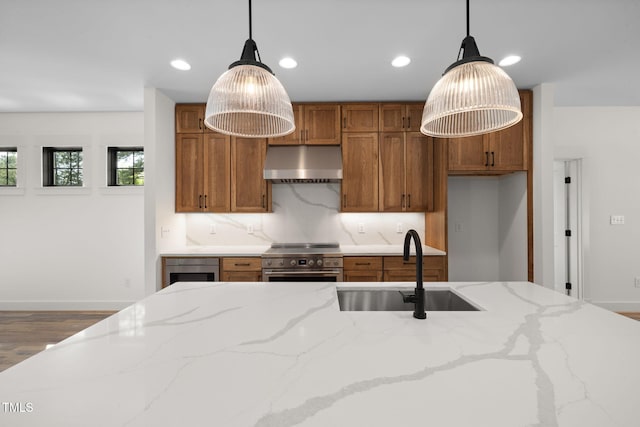 kitchen featuring under cabinet range hood, a sink, decorative light fixtures, high end stainless steel range, and brown cabinetry