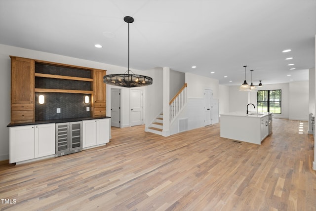 kitchen with tasteful backsplash, a chandelier, a sink, light wood finished floors, and beverage cooler