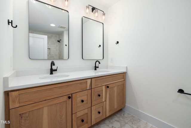 bathroom featuring baseboards, double vanity, a sink, and a tile shower