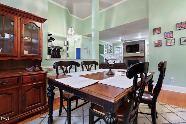 dining room with baseboards, light wood finished floors, ceiling fan, crown molding, and a brick fireplace