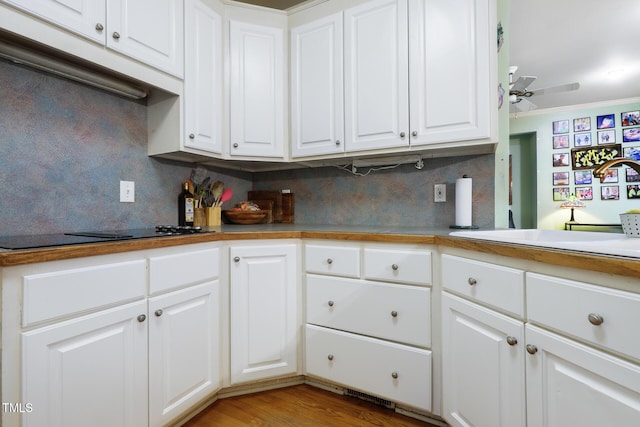 kitchen featuring a sink, black electric stovetop, backsplash, and white cabinetry