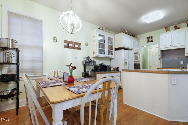 kitchen with white appliances, white cabinets, glass insert cabinets, light wood-style floors, and a chandelier