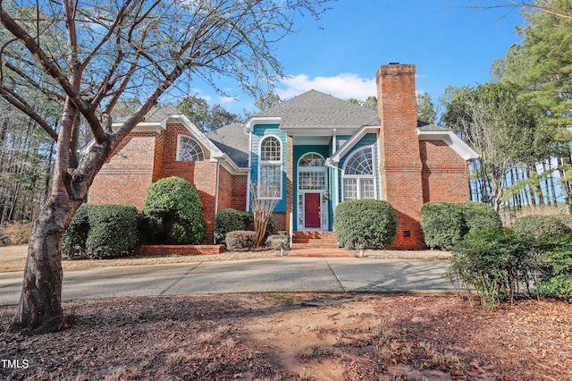 view of front of home featuring concrete driveway, a chimney, brick siding, and roof with shingles