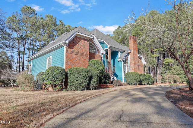 view of property exterior with brick siding, driveway, a chimney, and a shingled roof