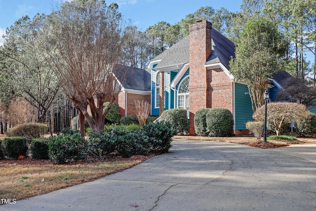 view of property exterior with brick siding, a chimney, and a shingled roof