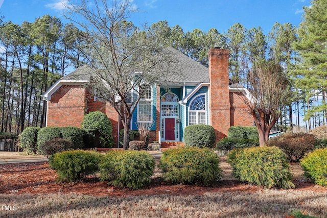 view of front facade with brick siding, a chimney, and a shingled roof