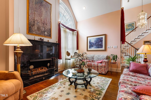 living area with wood finished floors, baseboards, high vaulted ceiling, stairs, and a tiled fireplace