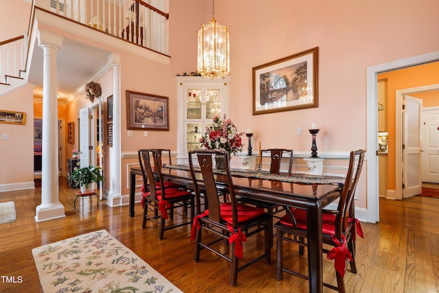 dining room with hardwood / wood-style floors, an inviting chandelier, decorative columns, and a towering ceiling