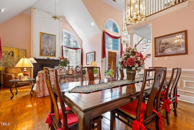 dining space with wainscoting, high vaulted ceiling, stairs, and wood finished floors