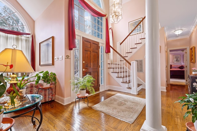 foyer featuring wood finished floors, stairway, a high ceiling, decorative columns, and baseboards