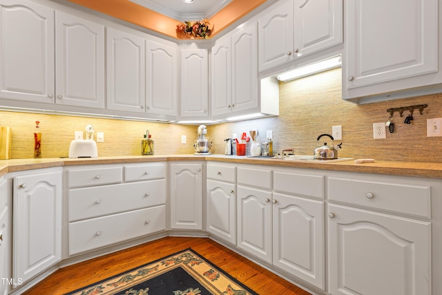 kitchen with backsplash, crown molding, white cabinetry, and light wood-type flooring