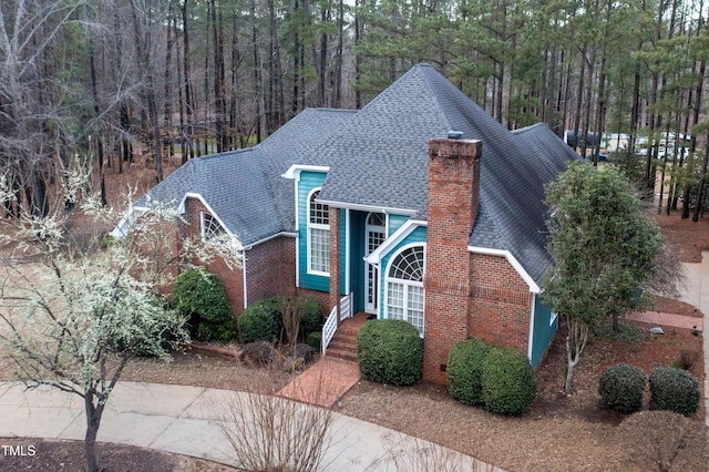 view of front of house featuring brick siding, roof with shingles, and a chimney