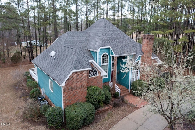 view of front of home featuring brick siding, roof with shingles, and a chimney