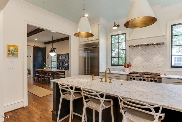 kitchen with built in fridge, light stone counters, dark wood finished floors, decorative backsplash, and a barn door