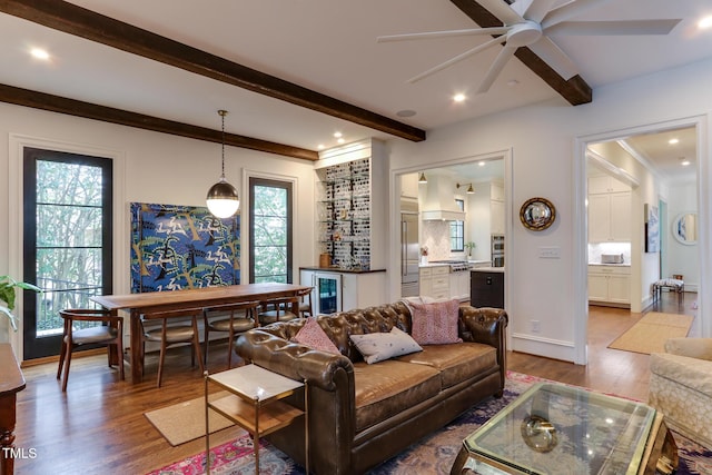 living room with beverage cooler, beamed ceiling, wood finished floors, and bar