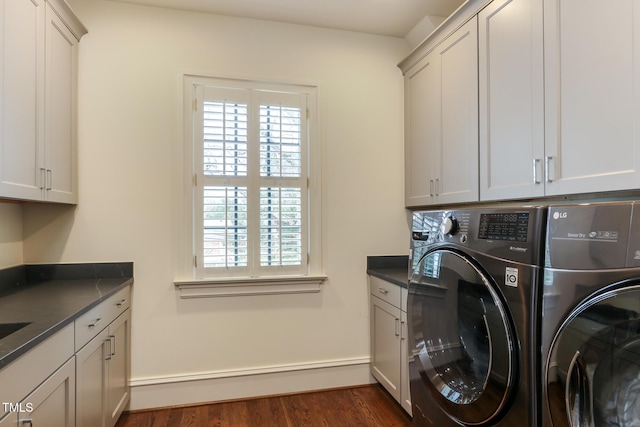 clothes washing area featuring dark wood-type flooring, washing machine and clothes dryer, and cabinet space