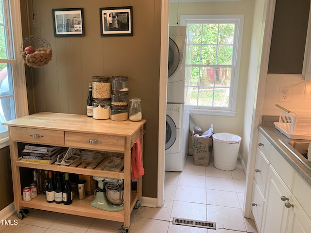 laundry area featuring light tile patterned floors, laundry area, visible vents, baseboards, and stacked washing maching and dryer