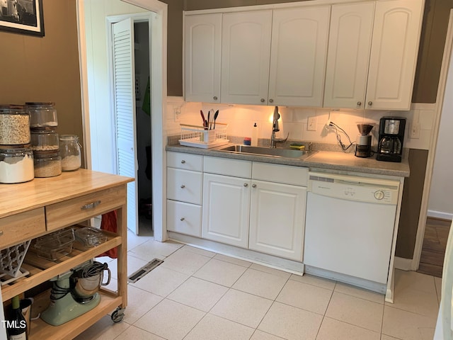 kitchen with white dishwasher, a sink, white cabinets, and decorative backsplash