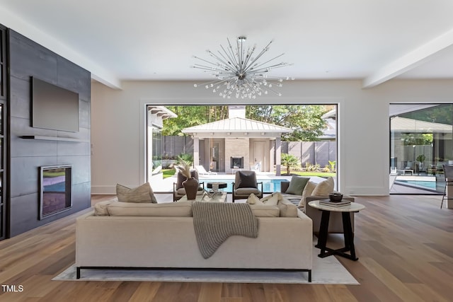 living room with a tiled fireplace, beam ceiling, wood finished floors, and a chandelier