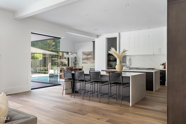 kitchen featuring a breakfast bar area, light countertops, light wood-style floors, white cabinetry, and a sink