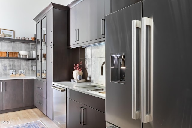 kitchen featuring light wood-style flooring, open shelves, stainless steel appliances, light countertops, and decorative backsplash