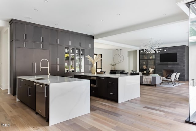 kitchen featuring light countertops, beamed ceiling, light wood-style floors, and a center island with sink