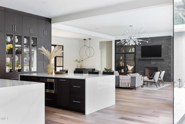 kitchen featuring light wood-type flooring, beam ceiling, light countertops, stainless steel oven, and dark cabinets