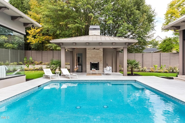 view of swimming pool with exterior fireplace, a ceiling fan, a patio, a fenced backyard, and a fenced in pool