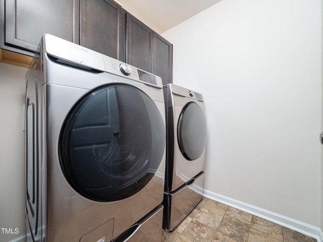 clothes washing area with washing machine and dryer, stone finish floor, cabinet space, and baseboards