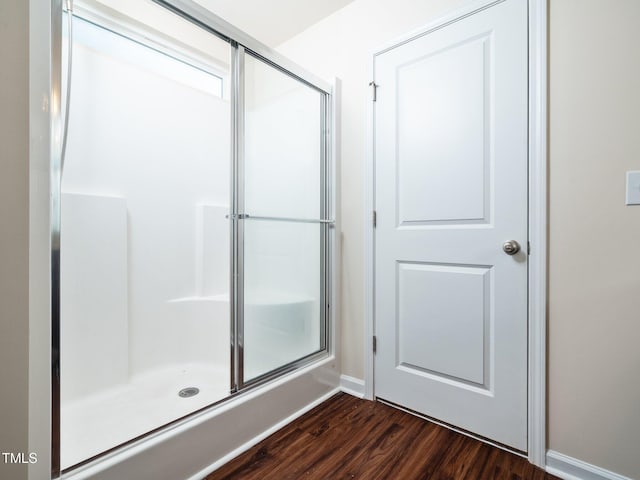 bathroom featuring wood finished floors, a shower with shower door, and baseboards