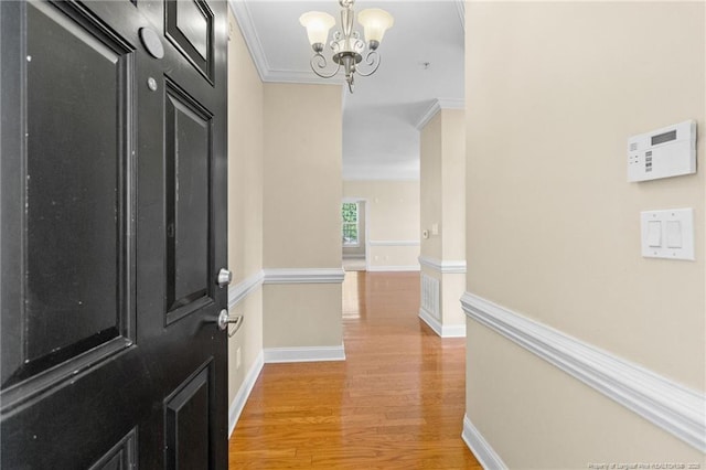 foyer entrance featuring light wood-style floors, baseboards, ornamental molding, and an inviting chandelier