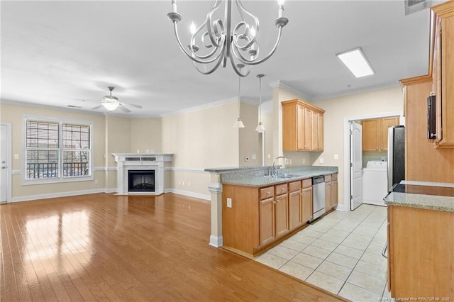 kitchen featuring light wood finished floors, appliances with stainless steel finishes, a fireplace with flush hearth, a sink, and washer / dryer