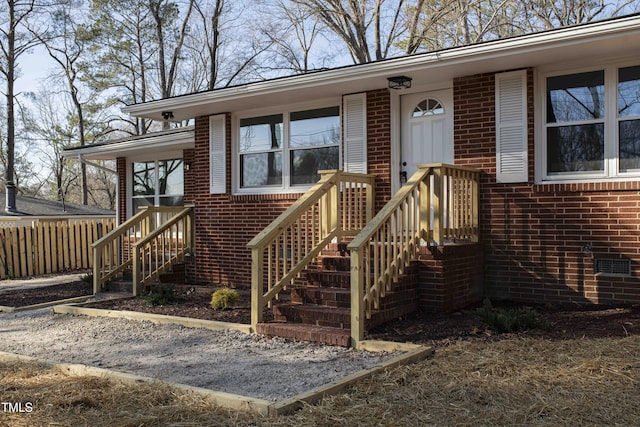 doorway to property featuring brick siding, crawl space, and fence