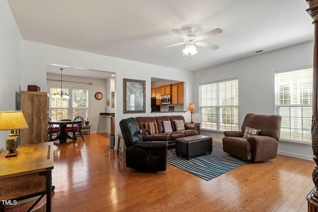 living area with hardwood / wood-style floors, ceiling fan with notable chandelier, visible vents, and baseboards