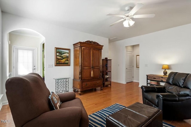 living room with light wood-style flooring, a ceiling fan, arched walkways, and baseboards