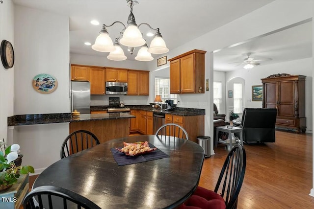 dining room with ceiling fan with notable chandelier, wood finished floors, and arched walkways