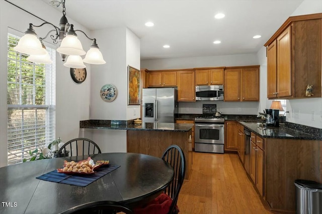 kitchen with dark stone countertops, a sink, stainless steel appliances, light wood-style floors, and brown cabinets