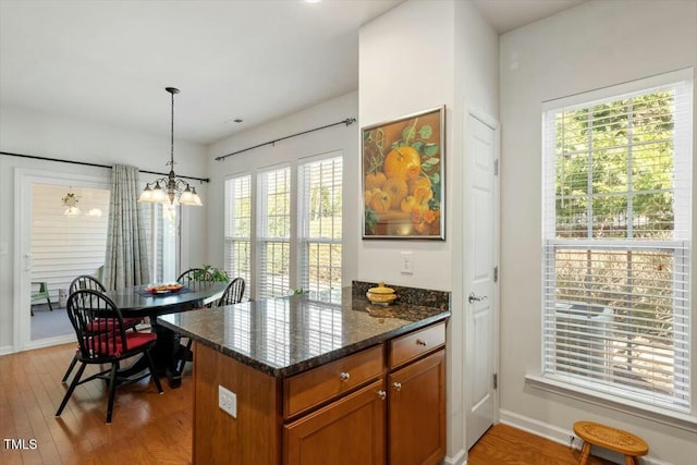 kitchen with dark stone counters, light wood-style flooring, brown cabinets, and pendant lighting