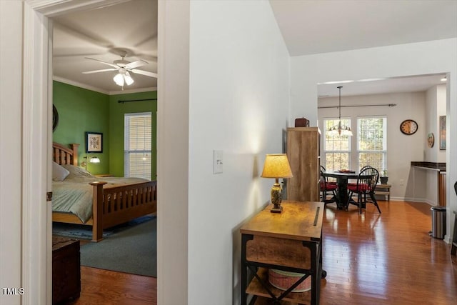 hall featuring crown molding, wood finished floors, baseboards, and a chandelier