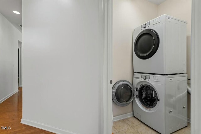 washroom featuring light tile patterned floors, laundry area, stacked washing maching and dryer, and baseboards