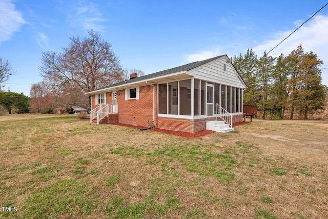 back of property featuring brick siding, a chimney, a lawn, entry steps, and a sunroom