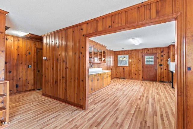 kitchen featuring light wood-style flooring, glass insert cabinets, brown cabinets, a textured ceiling, and wood walls